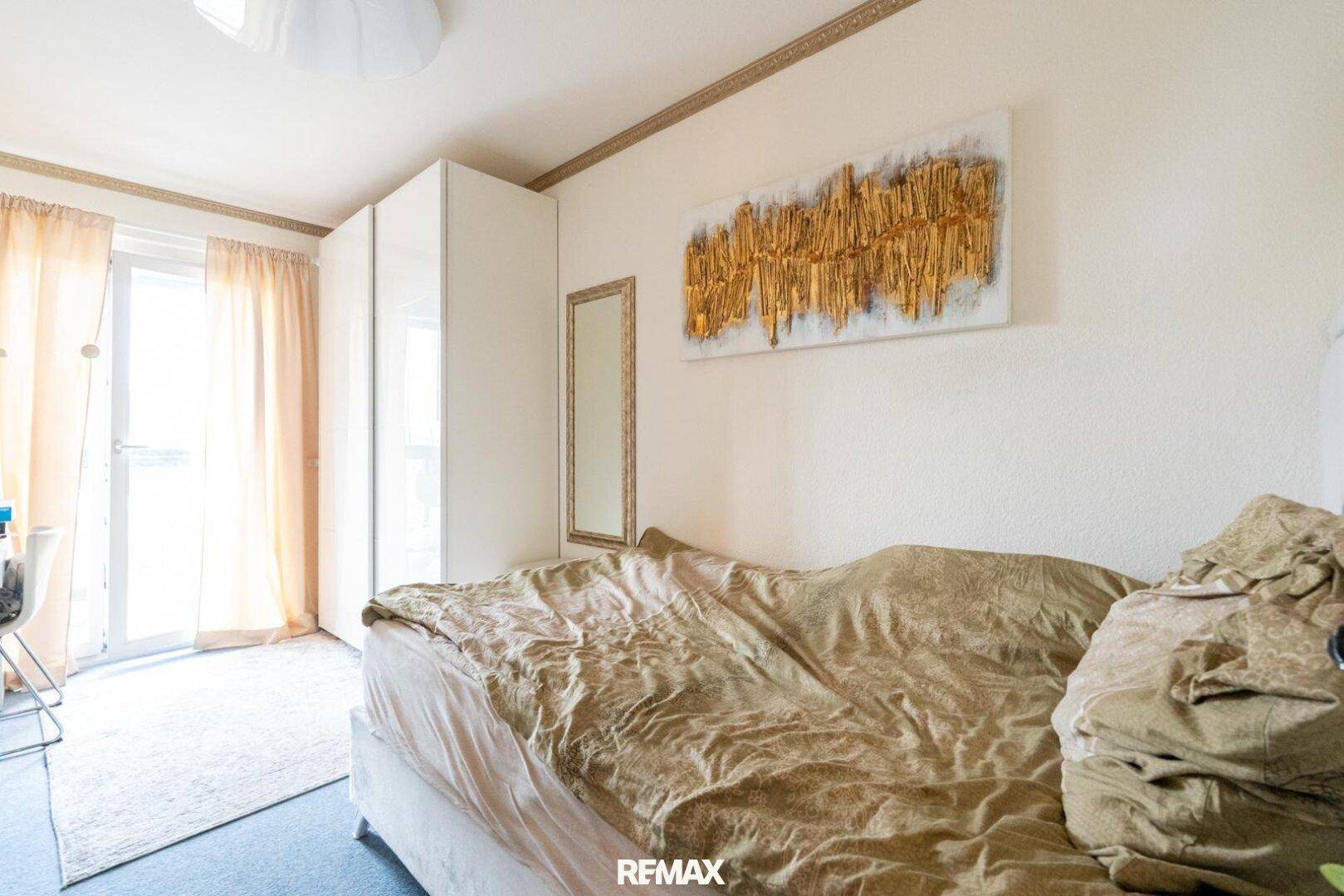 Helles Schlafzimmer mit Bett, Kleiderschrank und Zugang zu einem Balkon.