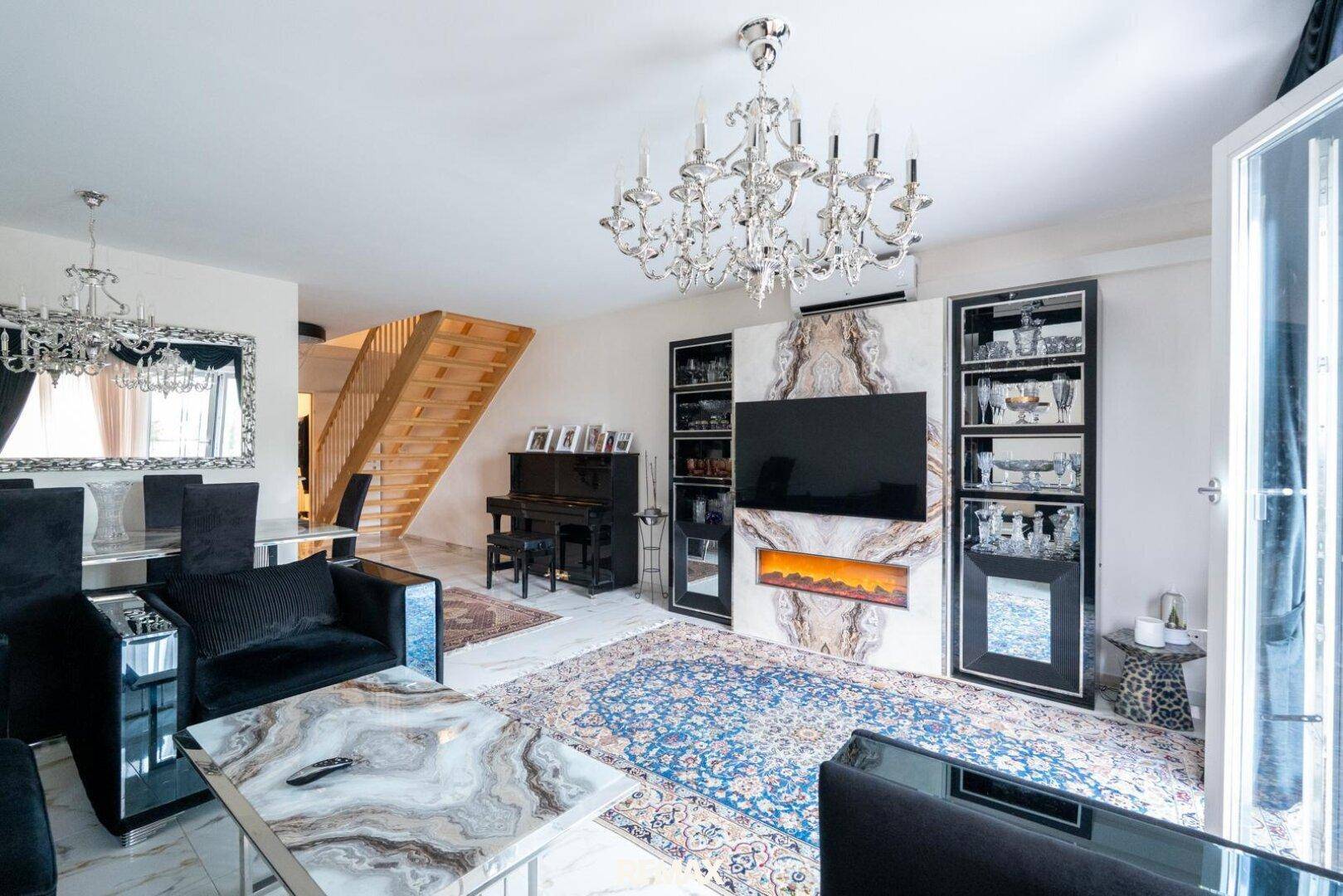 Elegantes Wohnzimmer mit Kronleuchter, Marmorboden und einem modernen Kamin unter dem Fernseher.