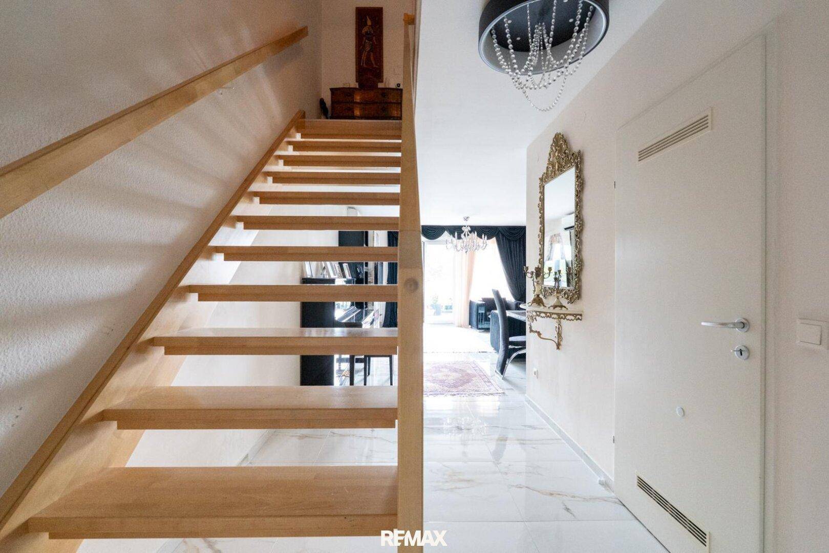 Heller Eingangsbereich mit Holztreppe, Marmorboden und einem dekorativen Spiegel.