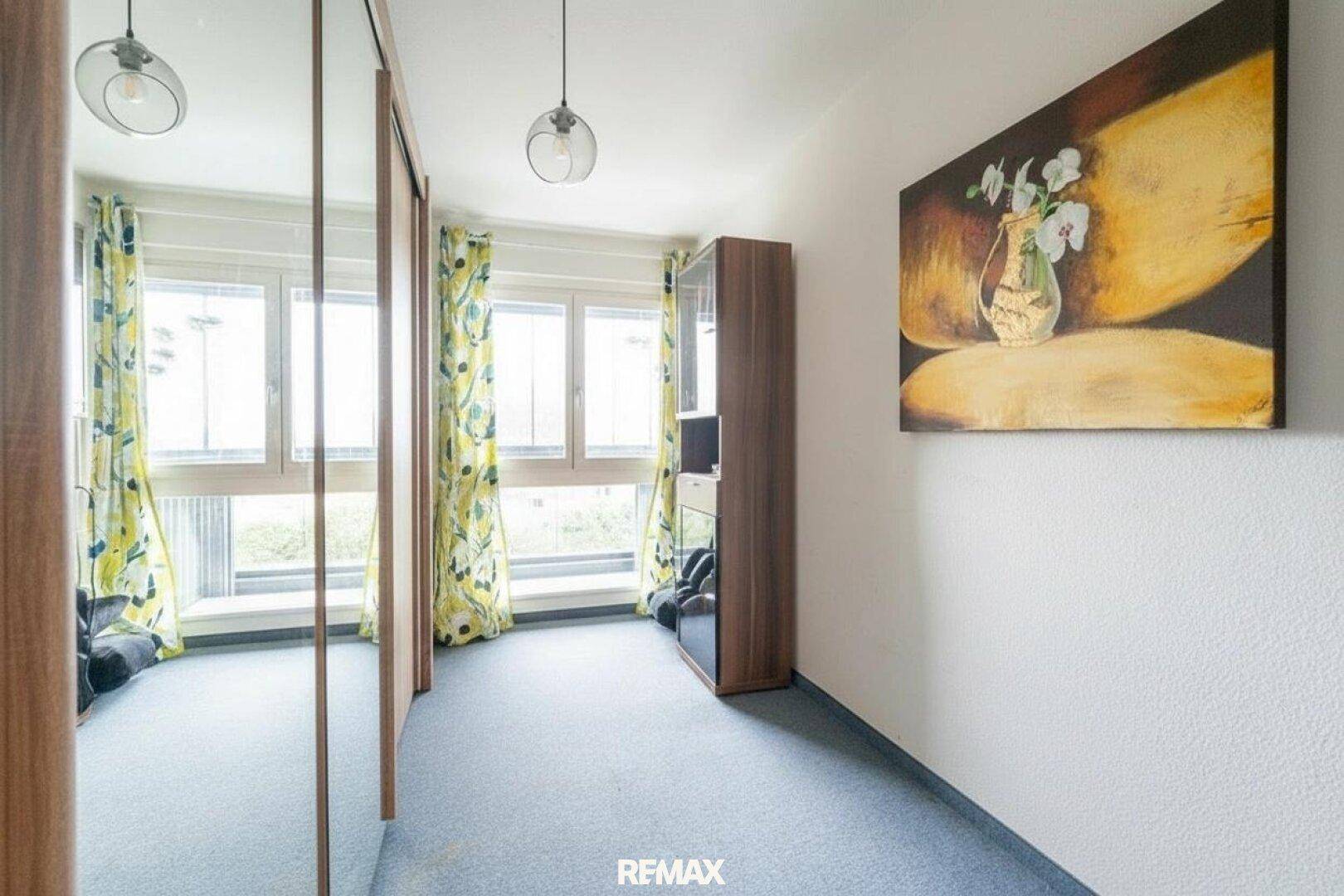 Schlafzimmer mit blauem Teppichboden, großen Fenstern und einem Kleiderschrank.