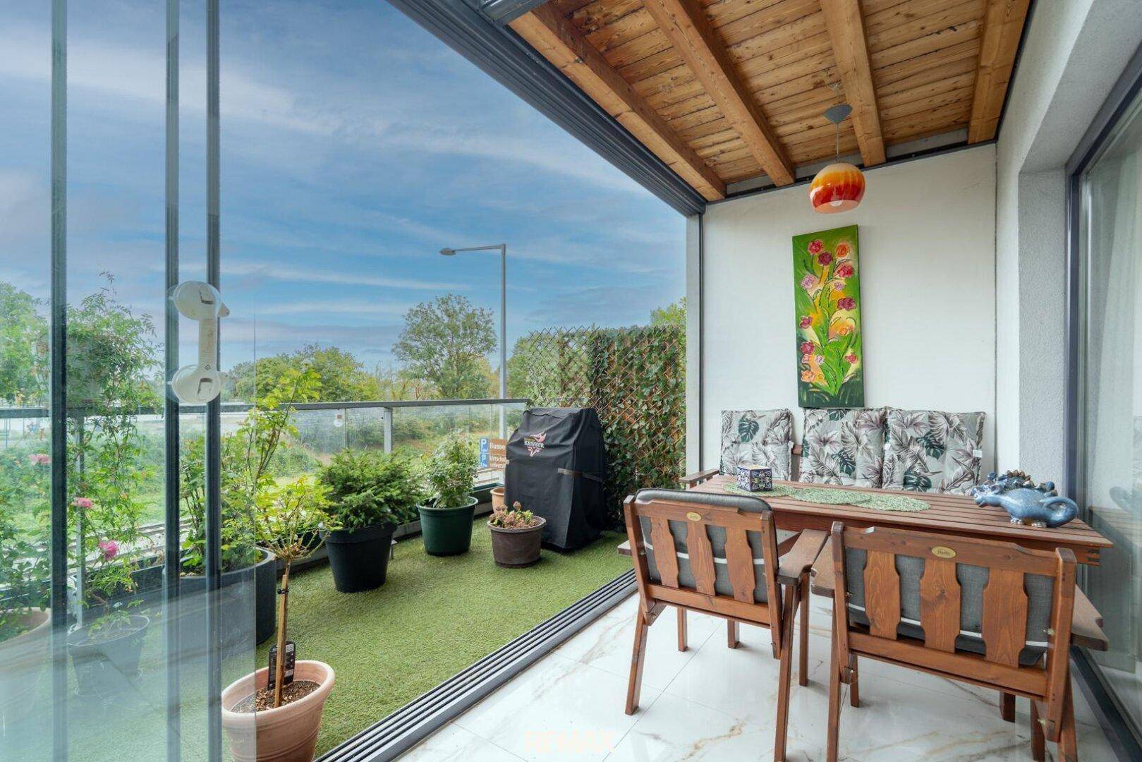 Gemütliche verglaste Loggia mit Essbereich, Kunstrasen und Pflanzen, ideal für Entspannung.