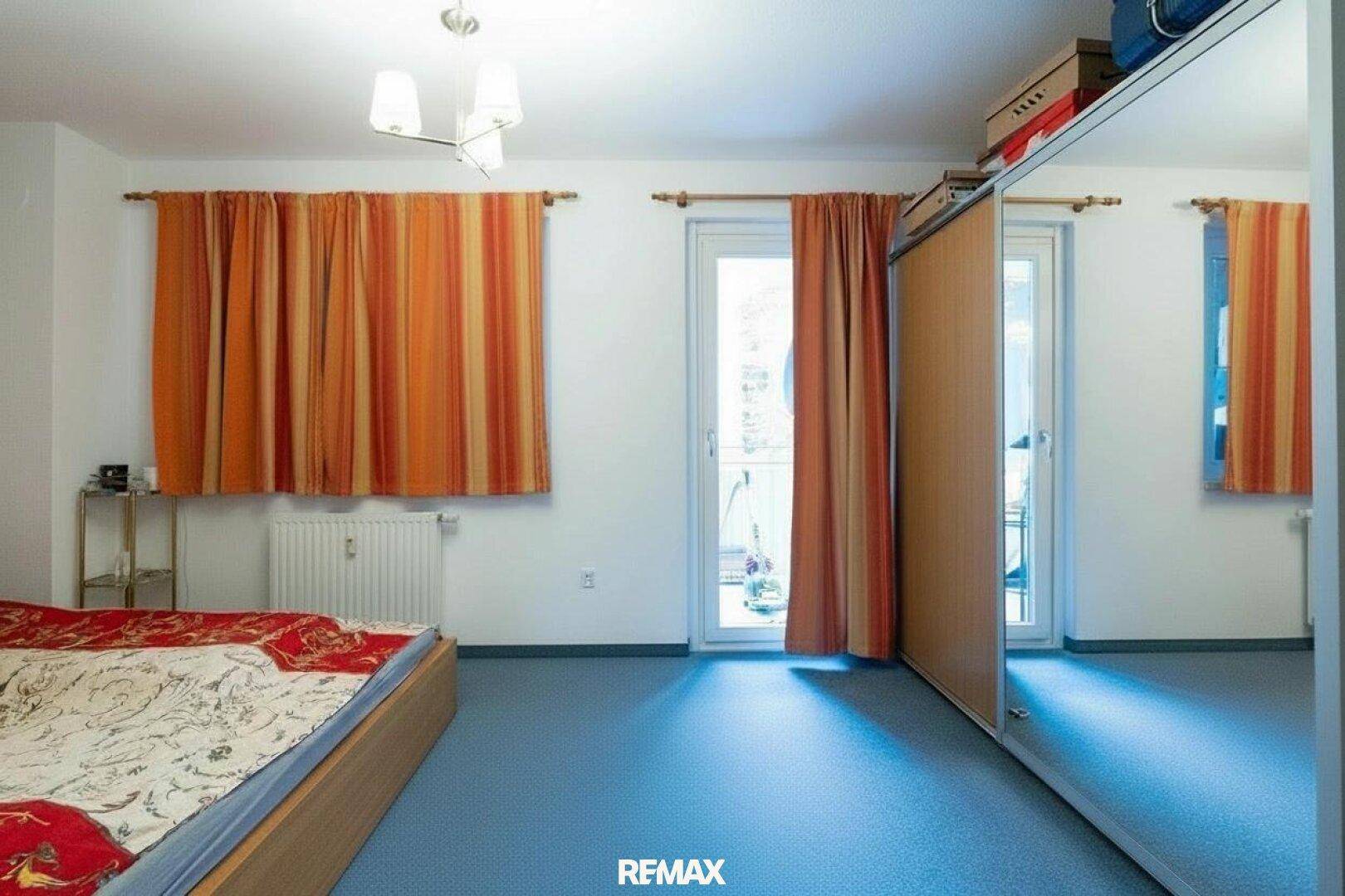 Schlafzimmer mit blauem Boden, orangefarbenen Vorhängen und Zugang zu einem Balkon.