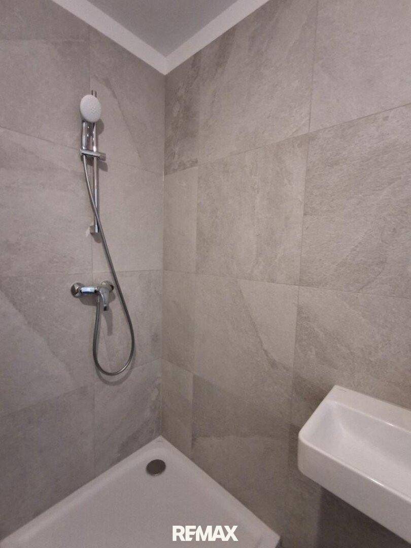 Duschbereich in einem modernen Badezimmer mit grauen Fliesen und Handbrause.
