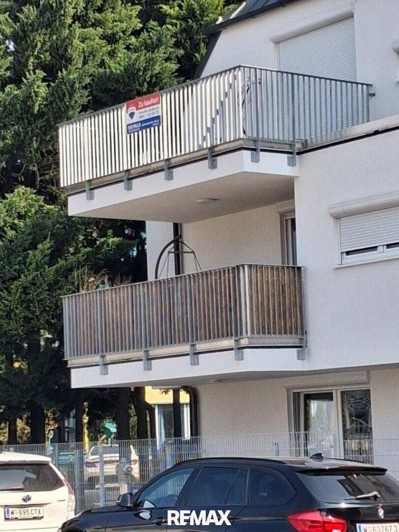 Detailansicht der modernen Fassade mit zwei Balkonen und "Zu kaufen"-Schild.