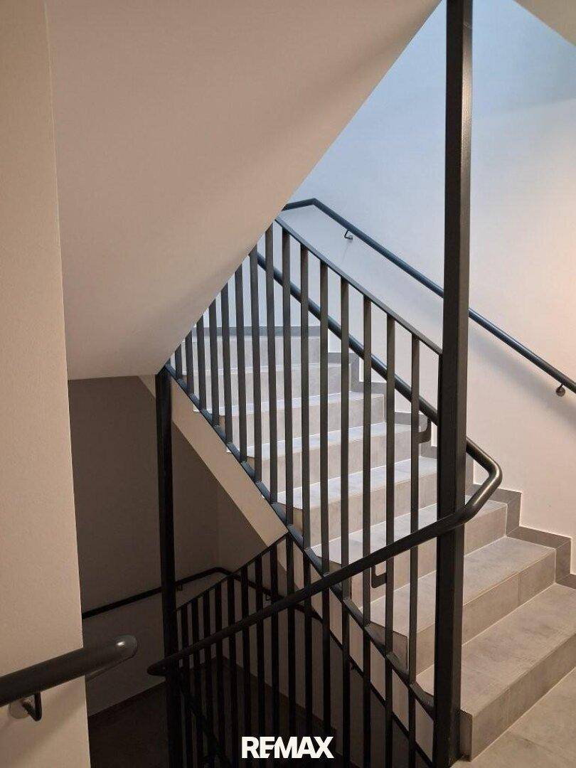 Modernes Treppenhaus mit Metallgeländer und gefliesten Stufen.