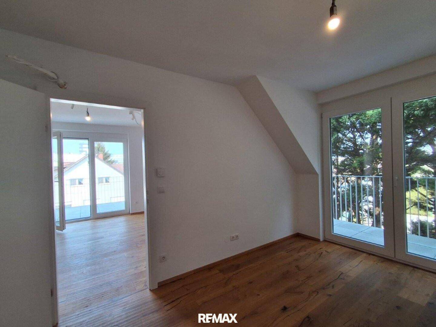 Leerer Raum mit Holzboden, Dachschräge und Zugang zu einem Balkon.