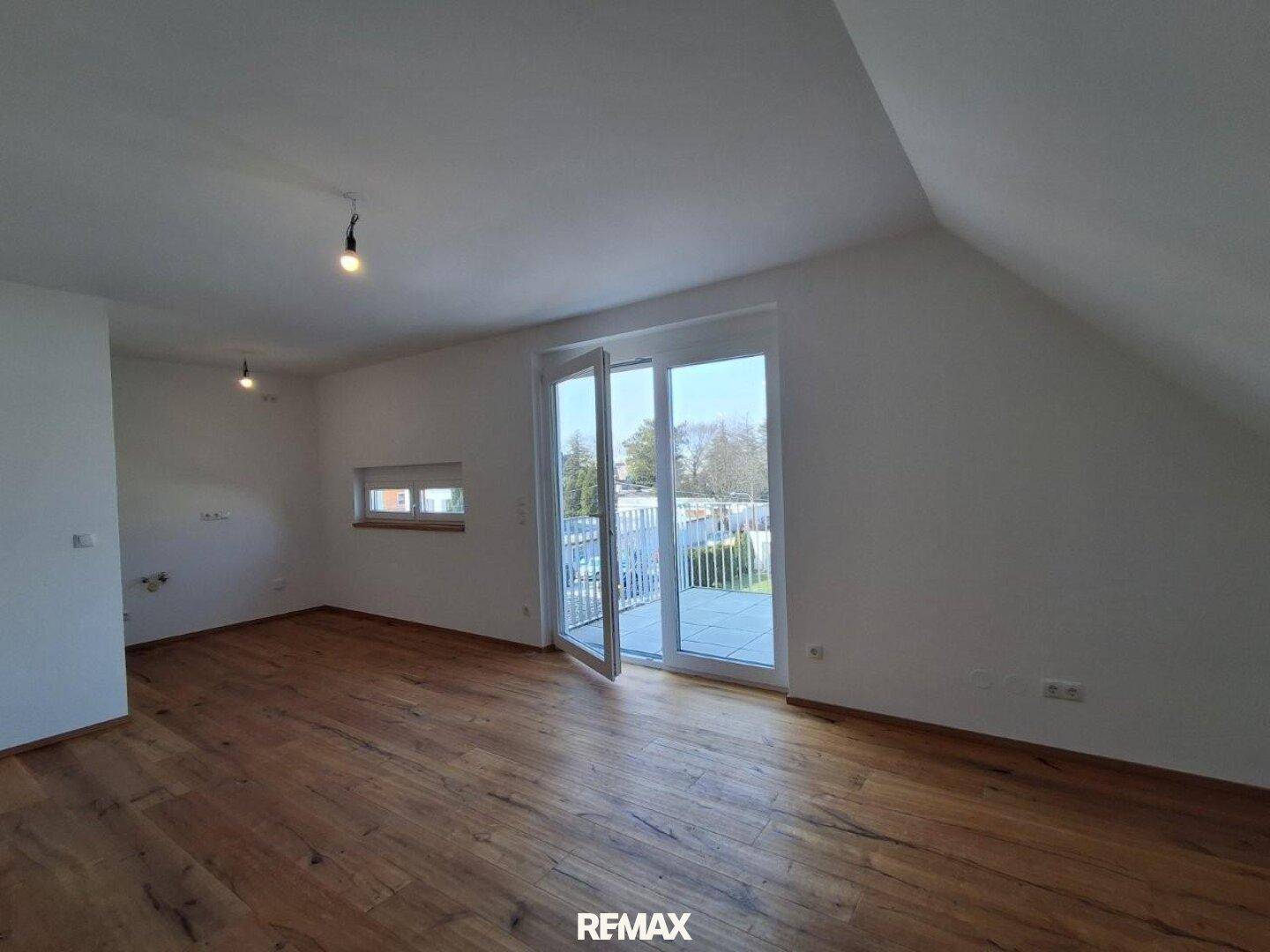 Heller, leerer Raum mit Holzboden und Zugang zu einem Außenbereich.