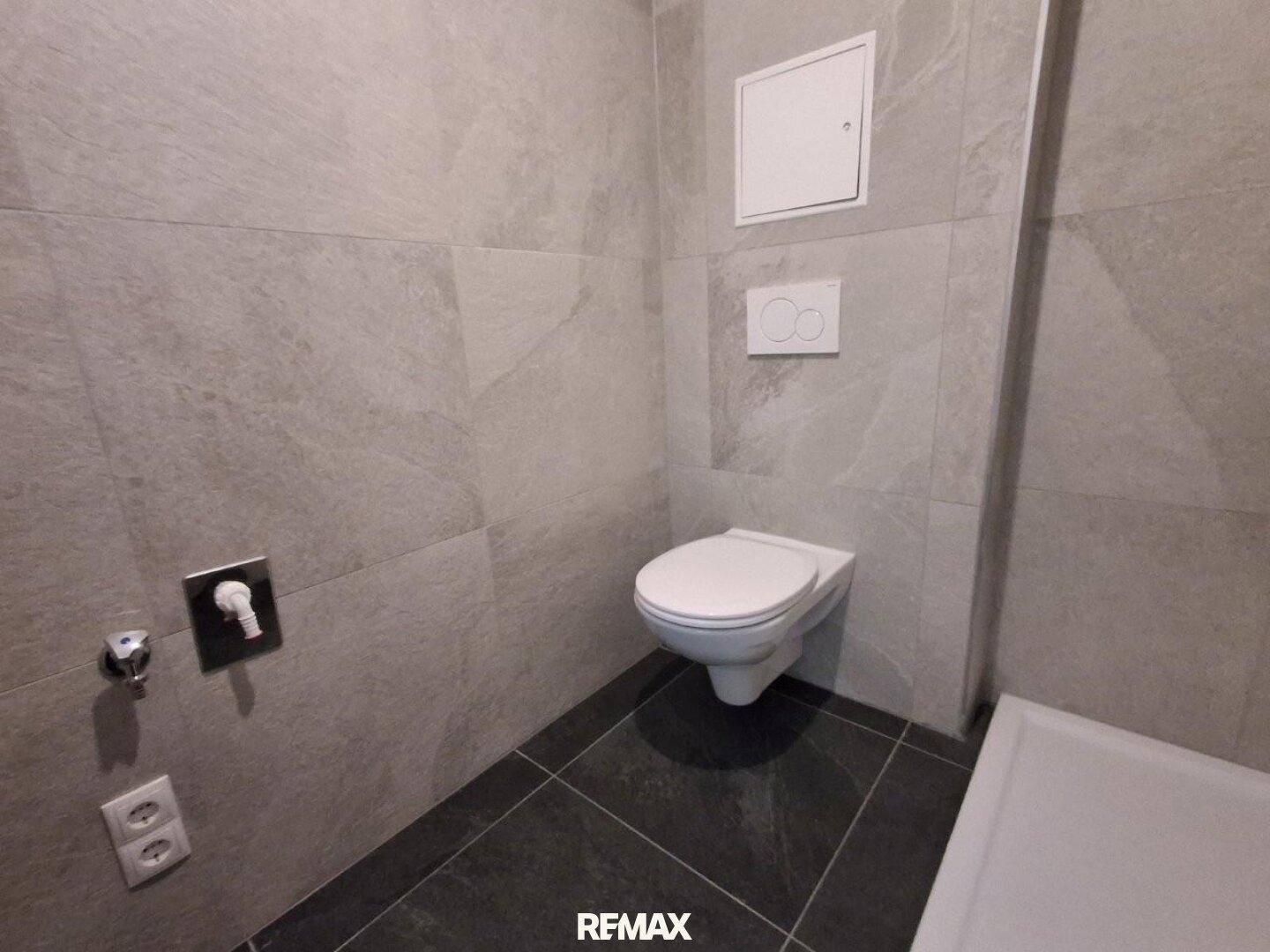 Modernes WC mit grauen Fliesen und wandhängender Toilette.