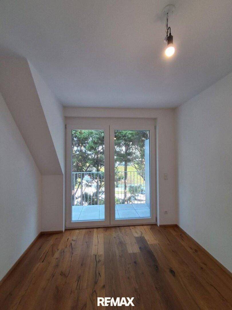 Helles Schlafzimmer mit Holzboden, Dachschräge und Balkonzugang.