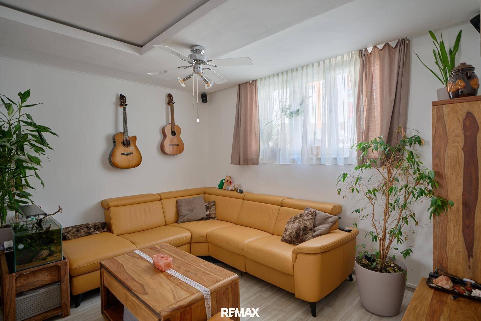 Gemütliches Wohnzimmer mit gelbem Ecksofa, Holzmöbeln und Deckenventilator.