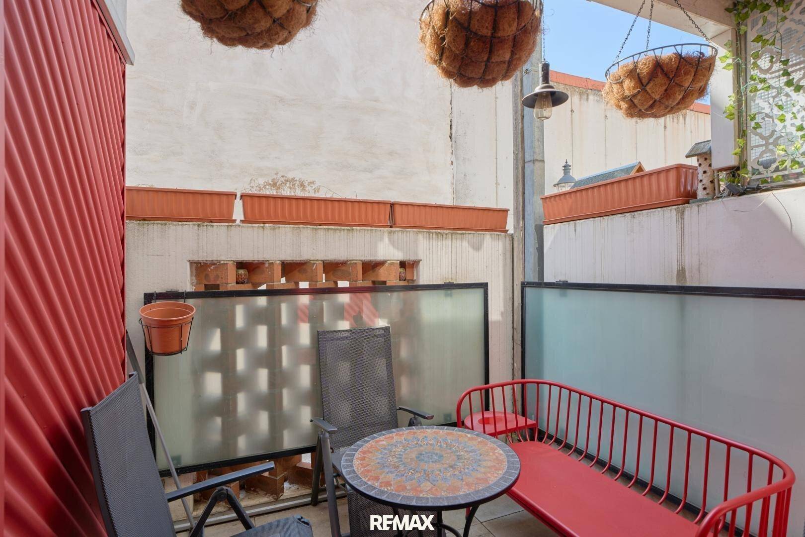 Kleine, möblierte Terrasse mit roter Bank und dekorativen Hängekörben.