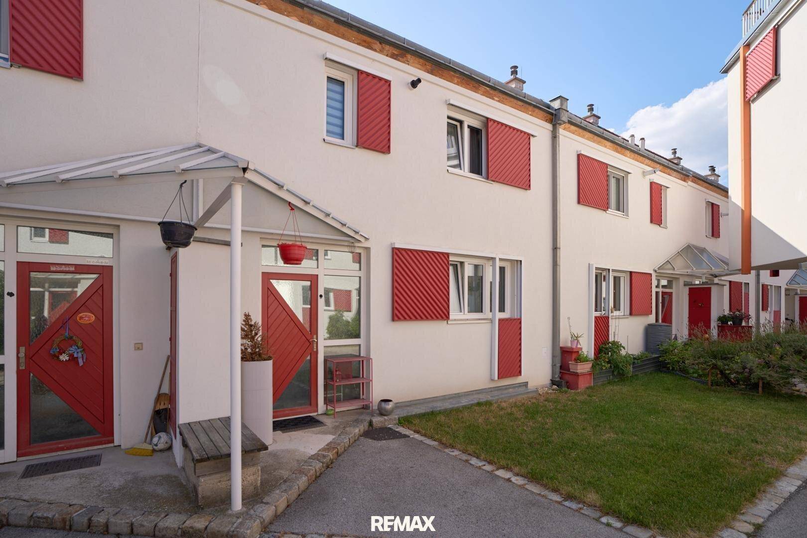 Reihe von Wohnhäusern mit roten Fensterläden und gepflegten Vorgärten.