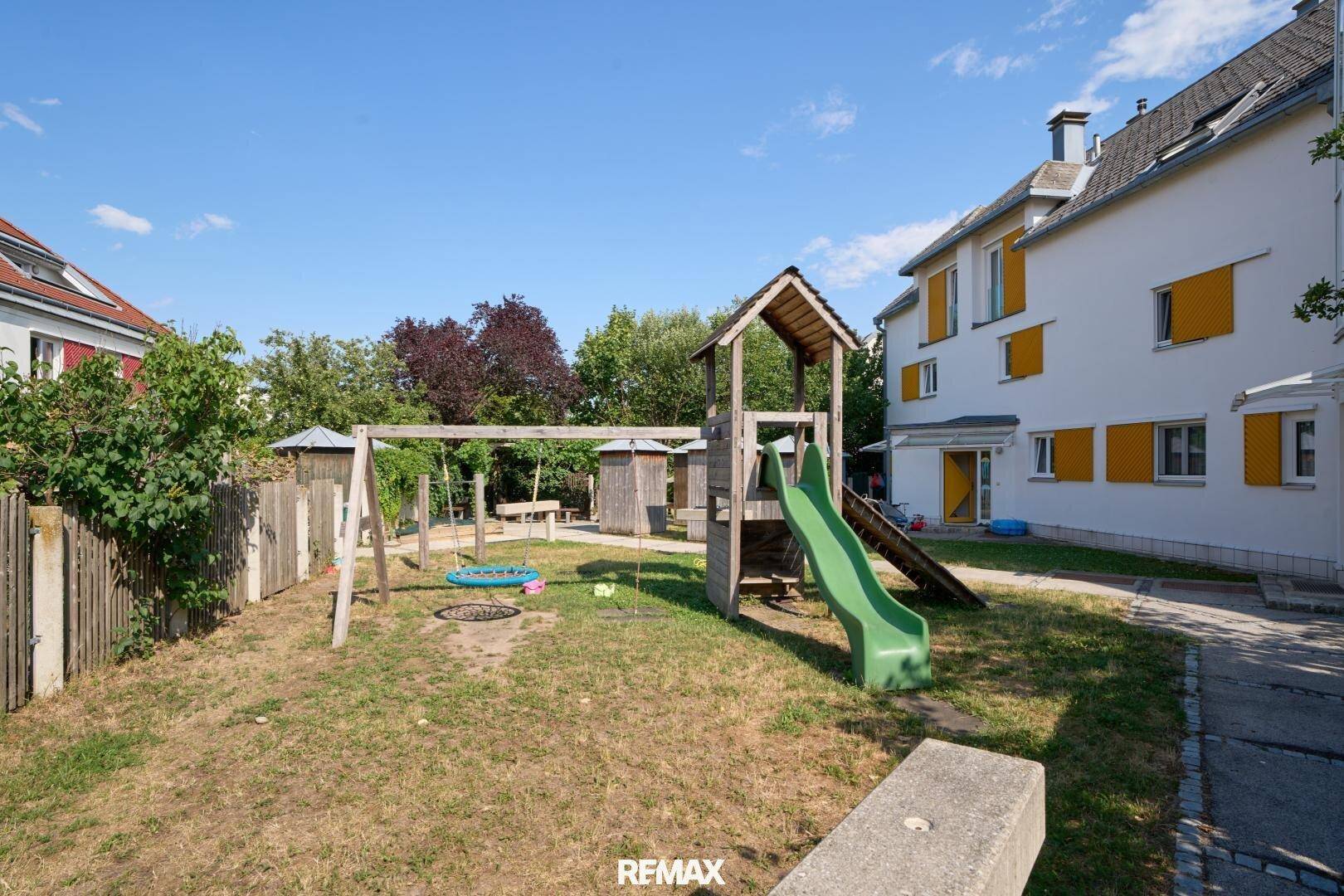 Gemeinschaftlicher Spielplatz mit Rutsche und Schaukeln in einer grünen Umgebung.
