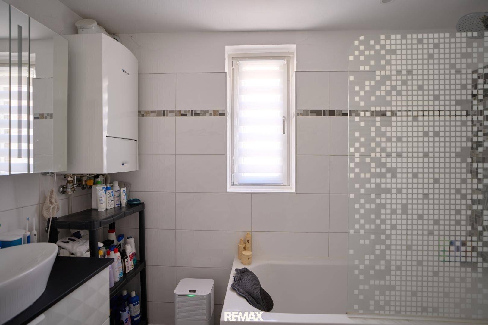Helles Badezimmer mit Badewanne, Fenster und modernen Fliesen.