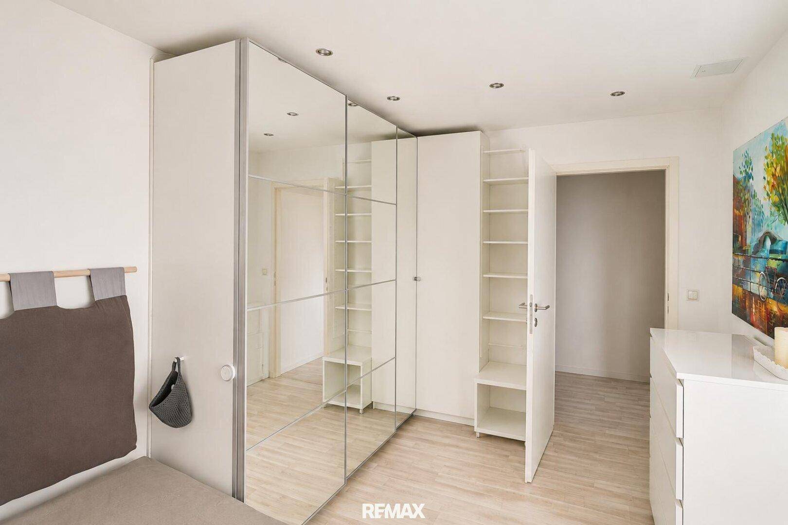 Schlafzimmer mit offenen Kleiderschränken und hellem Laminatboden.