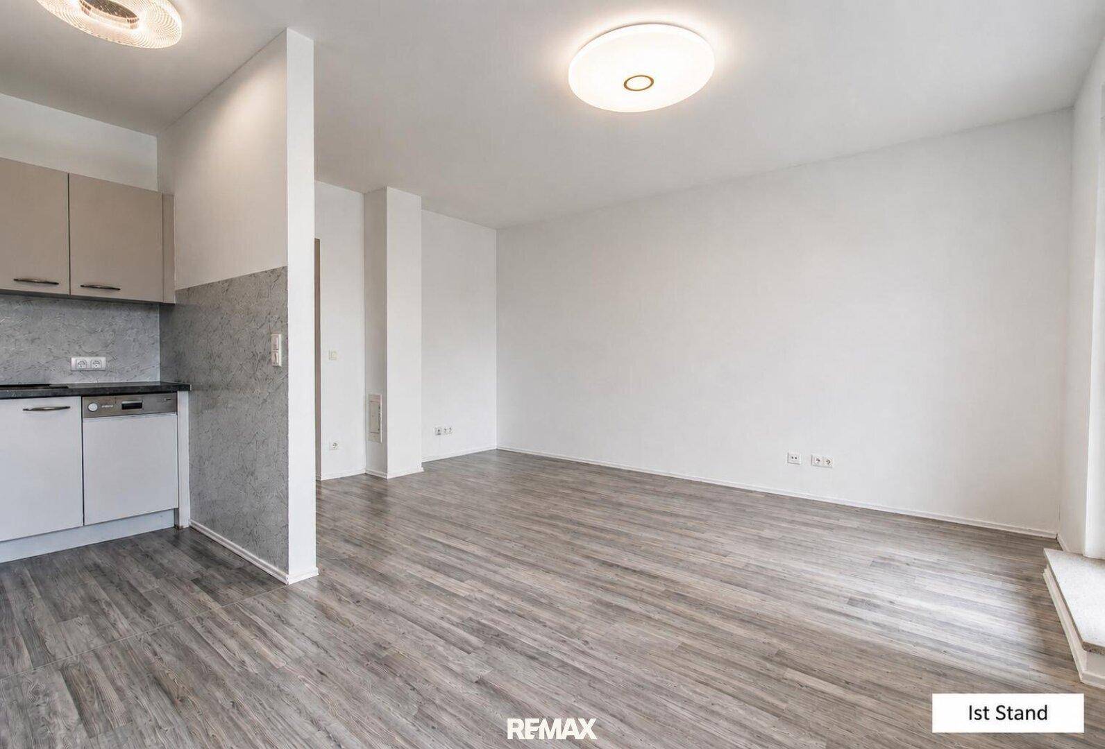 Geräumiger, unmöblierter Wohnbereich mit integrierter Küche und hellem Laminatboden.