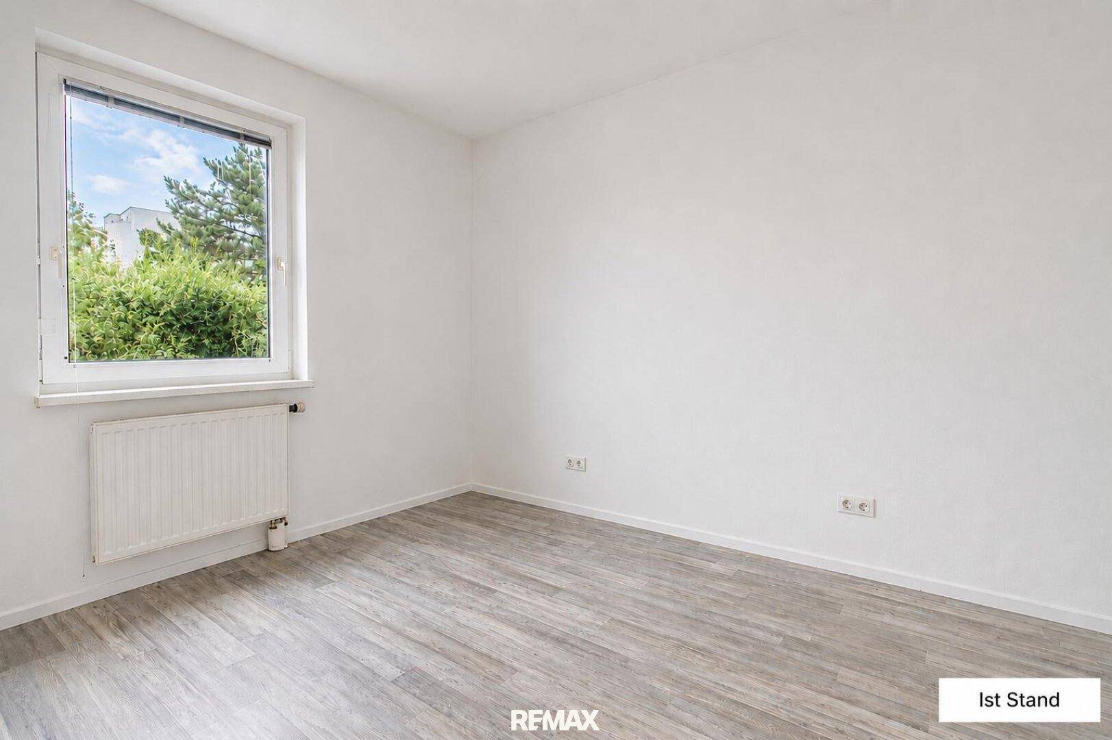 Unmöbliertes Schlafzimmer mit hellem Laminatboden und großem Fenster mit Blick ins Grüne.