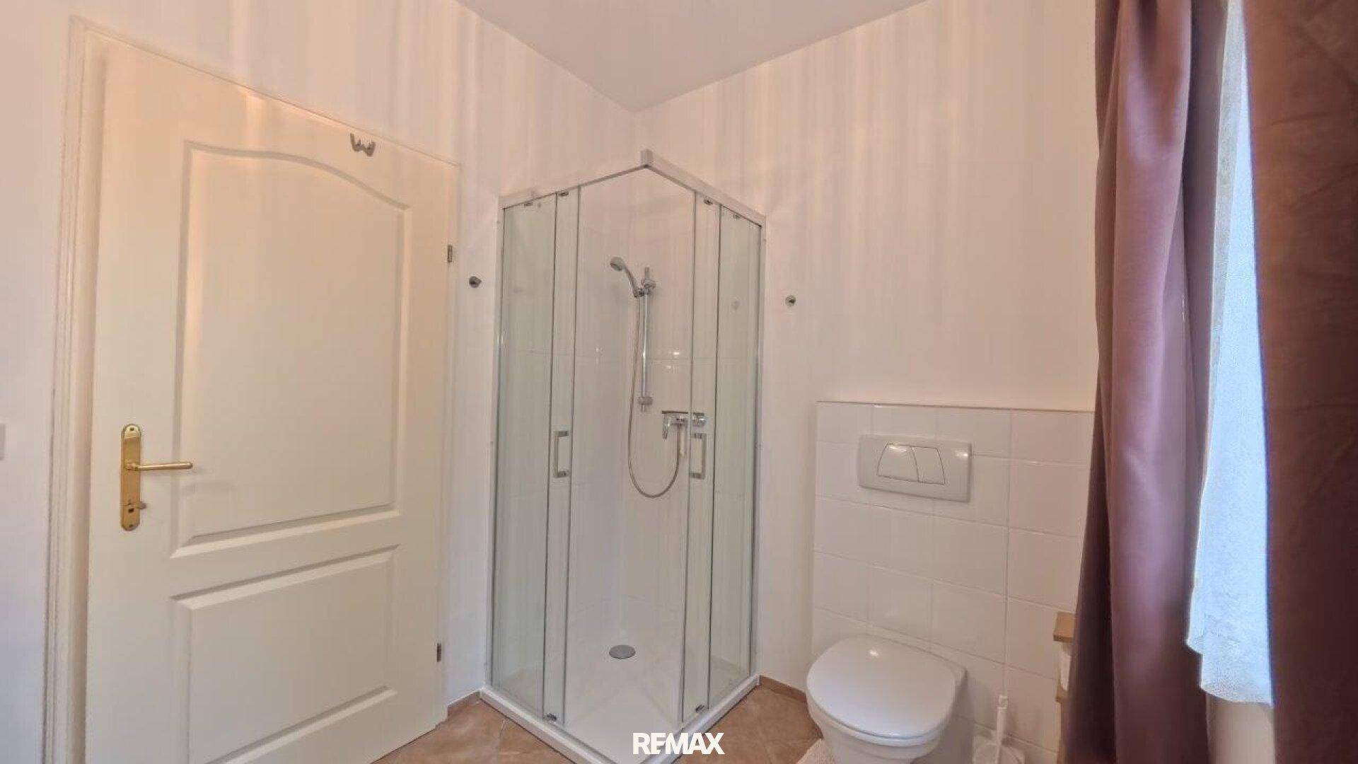 Badezimmer mit Eckdusche, Toilette und weißen Fliesen.