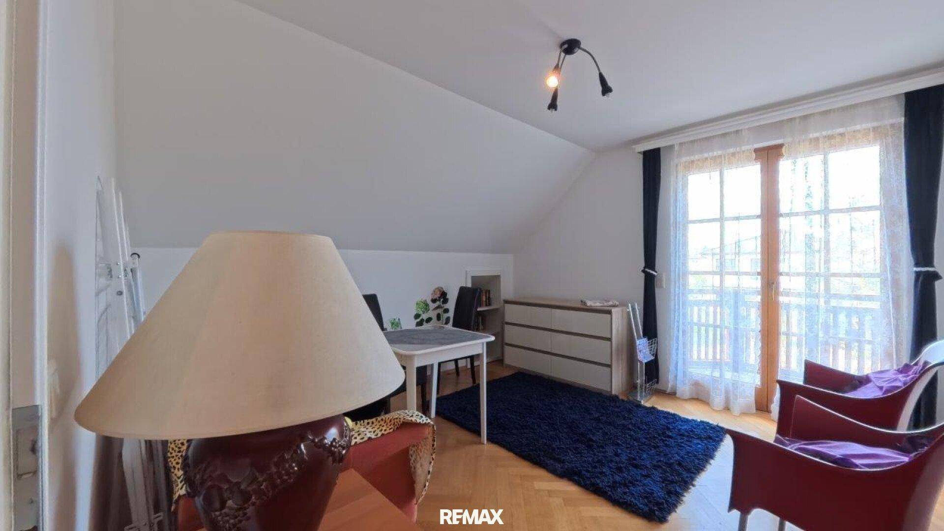 Zimmer im Dachgeschoss mit Teppich, Stühlen und Zugang zu einem französischen Balkon.