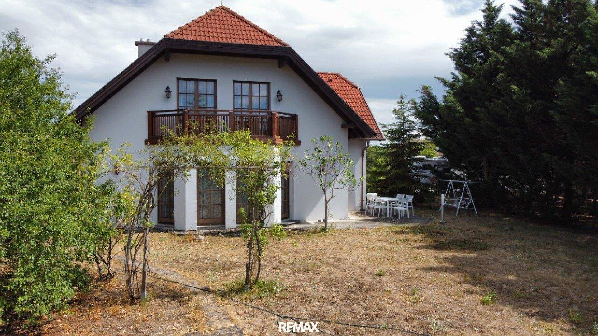 Haus mit großem Garten, Terrasse und Balkon, umgeben von viel Grün und Bäumen.
