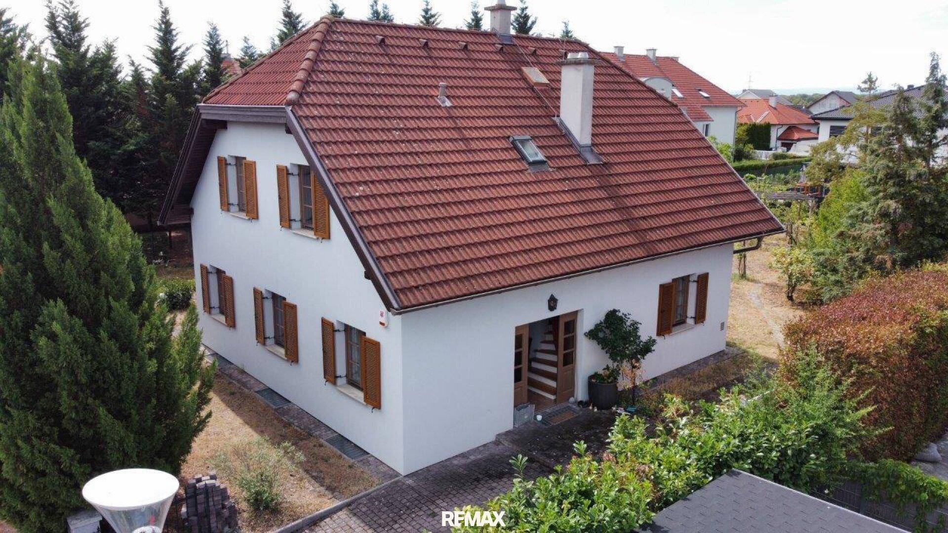 Freistehendes Einfamilienhaus mit rotem Ziegeldach, Holzfensterläden und gepflegtem Vorgarten.