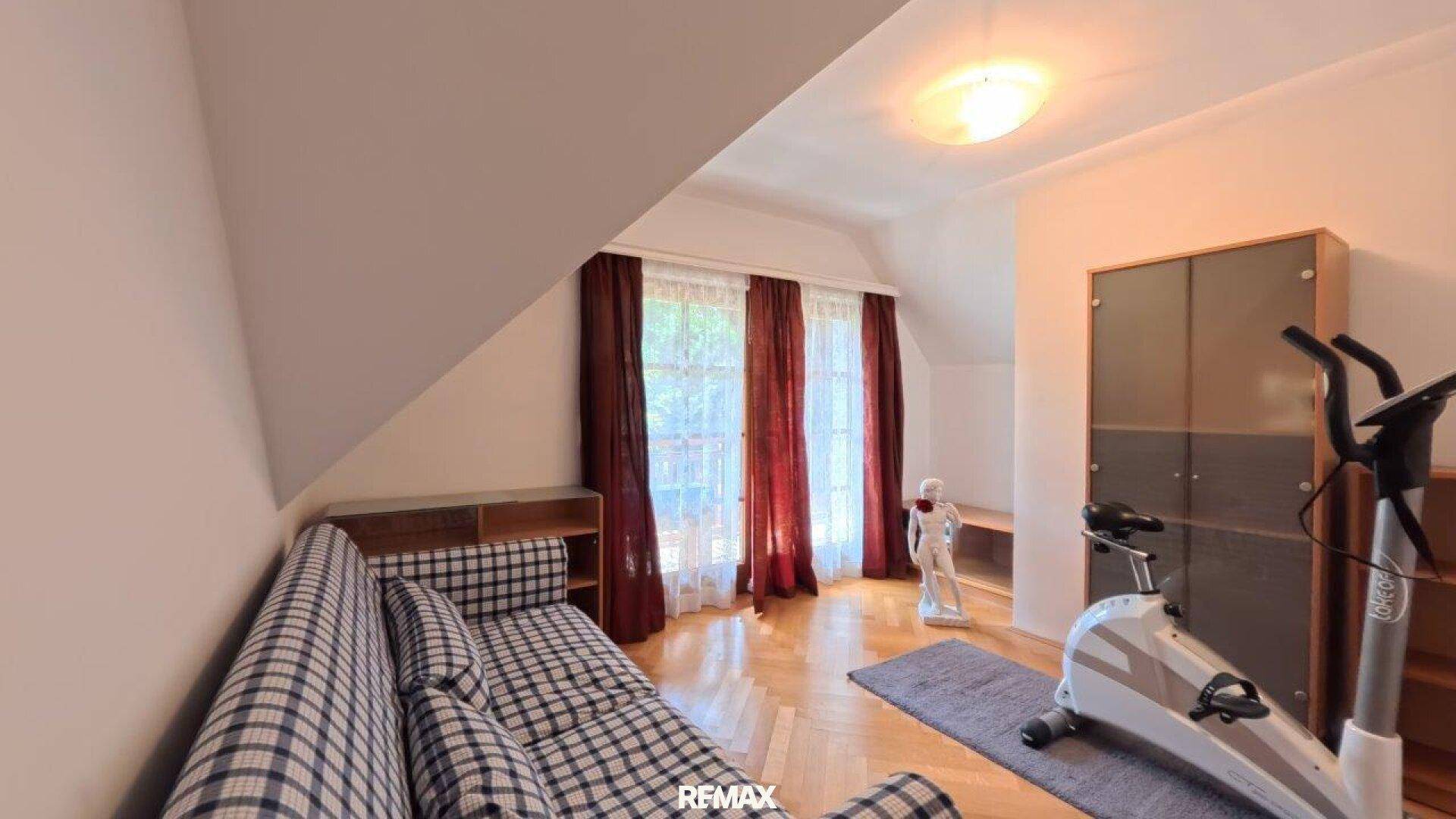 Dachgeschosszimmer mit Schlafsofa, Fitnessgerät und Fenster.