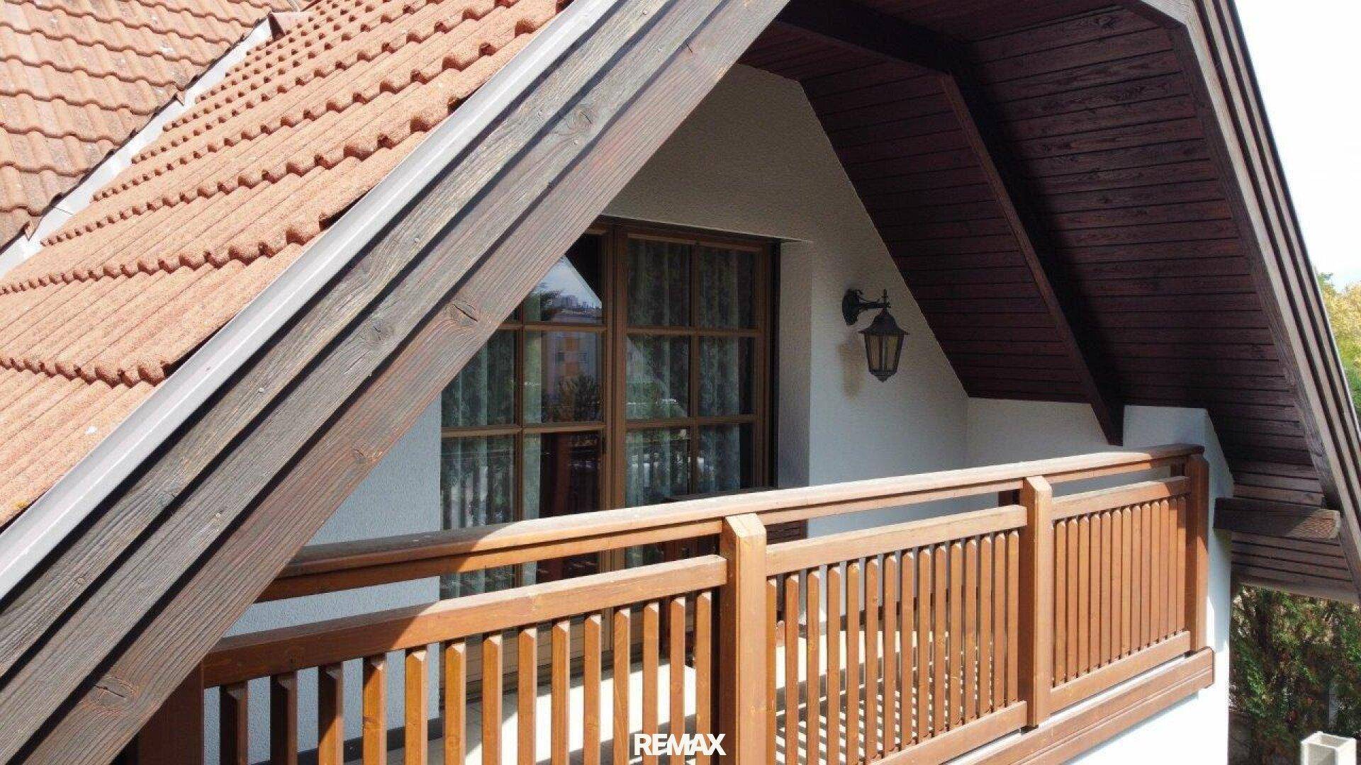 Holzbalkon mit traditionellem Geländer und Blick auf die grüne Umgebung unter einem Dachvorsprung.
