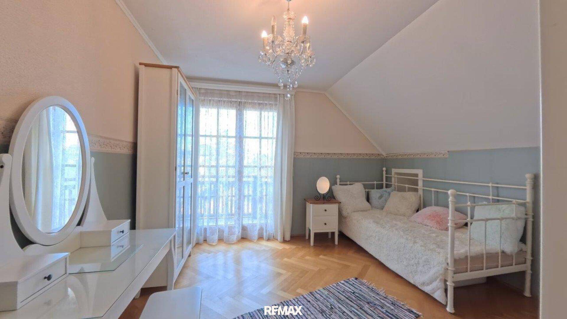 Helles Schlafzimmer im Dachgeschoss mit Einzelbett, Schminktisch und Balkonzugang.