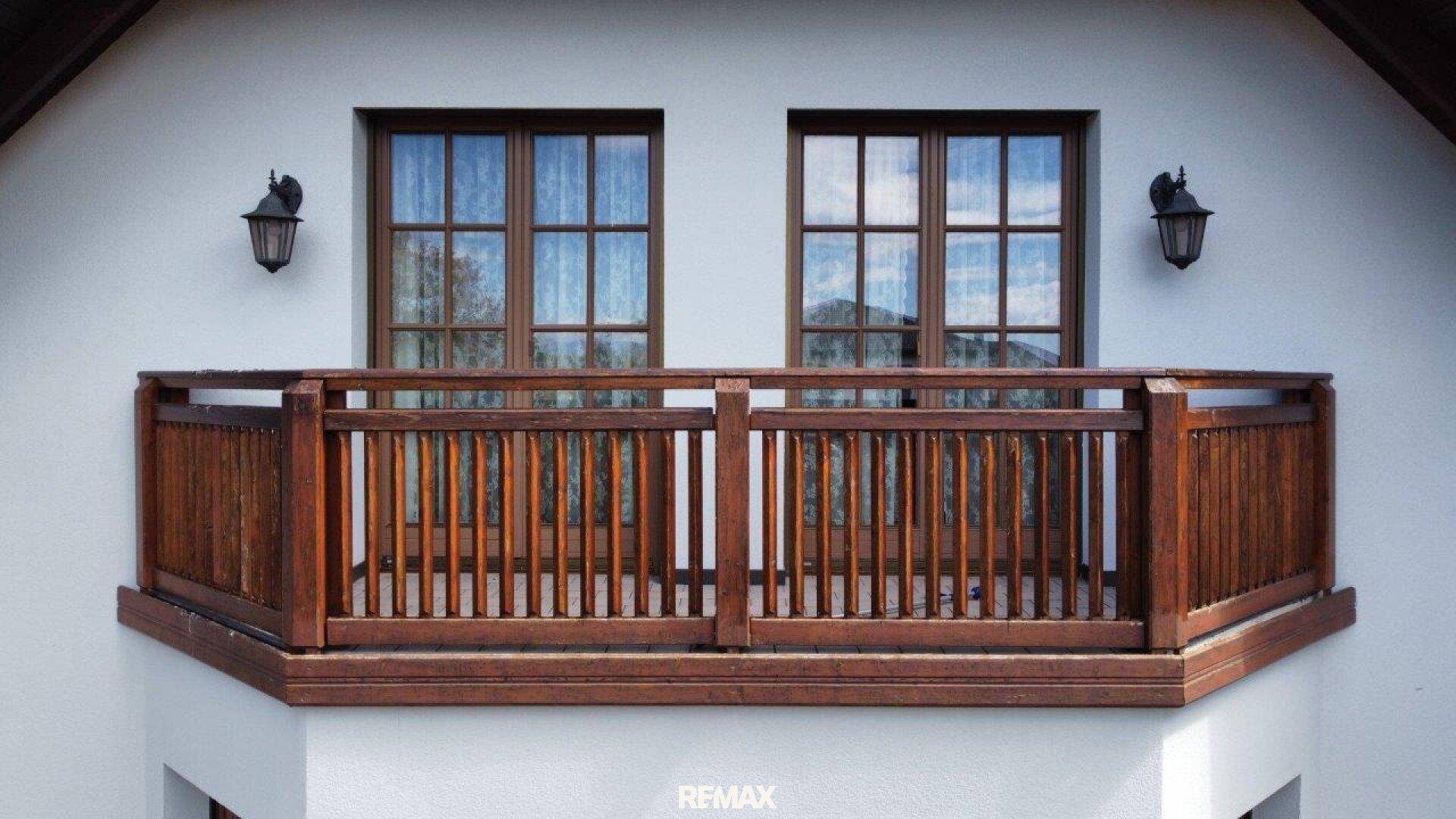 Frontansicht eines Holzbalons mit traditionellem Geländer und zwei Fenstern an der Hausfassade.