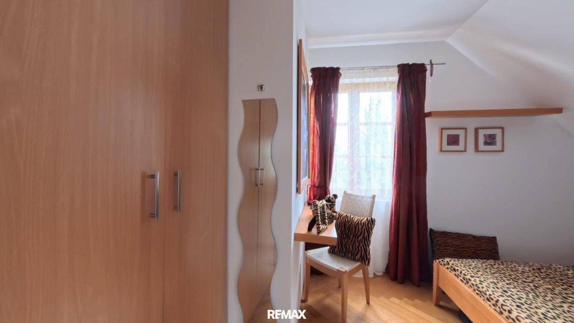 Schlafzimmer im Dachgeschoss mit Kleiderschrank, Schreibtisch und Fenster.