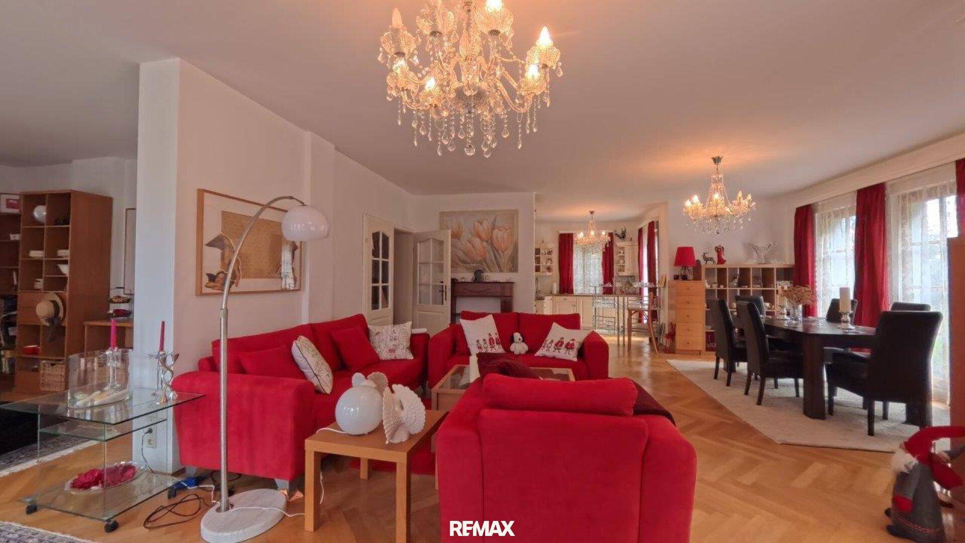 Großer offener Wohn- und Essbereich mit roten Sofas, Kronleuchtern und Parkettboden.
