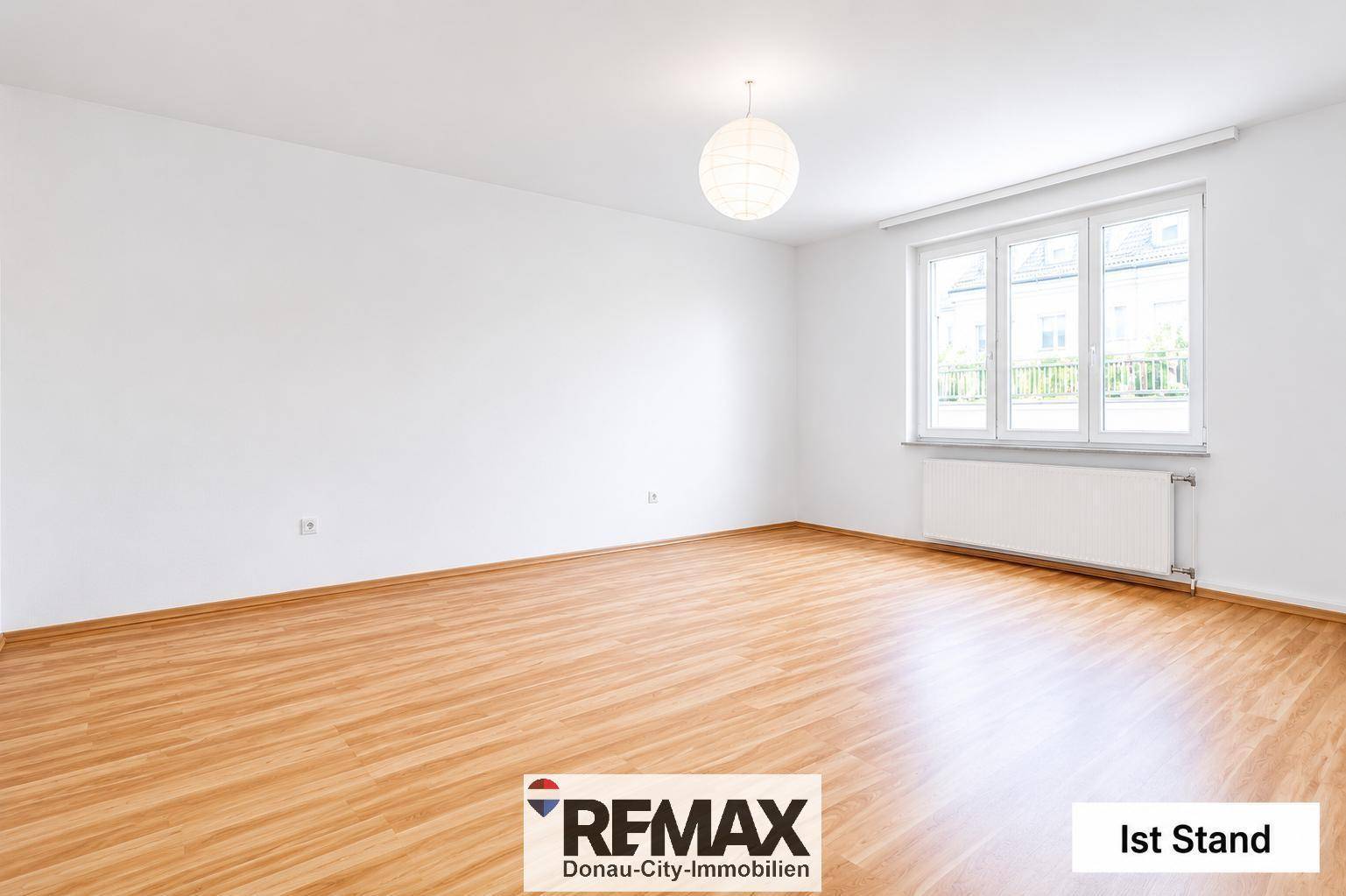 Leerer Wohnbereich mit großen Fenstern und hellem Laminatboden im Ist-Zustand.