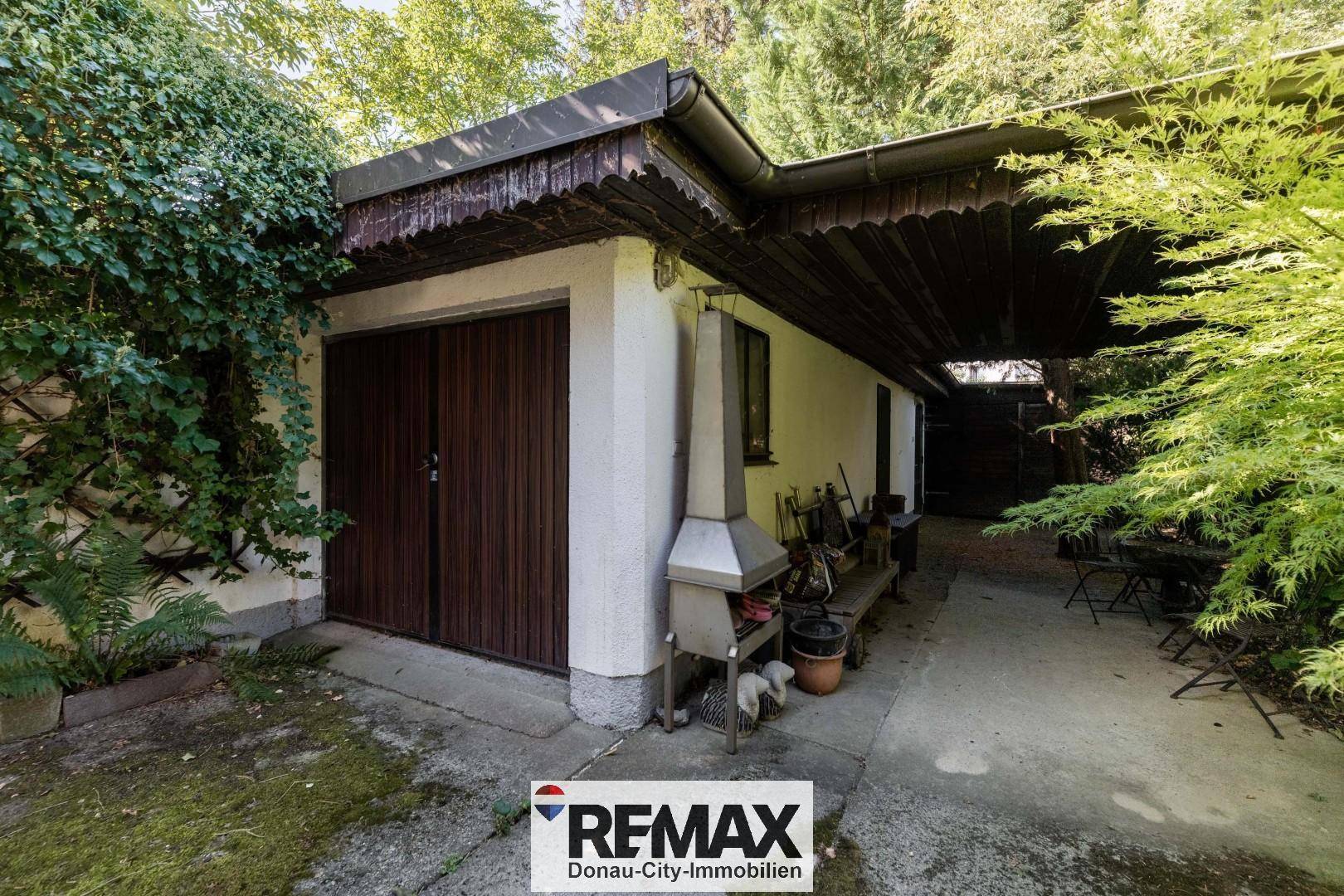 Garage mit Holztoren und angrenzendem Außenbereich mit Grillplatz.