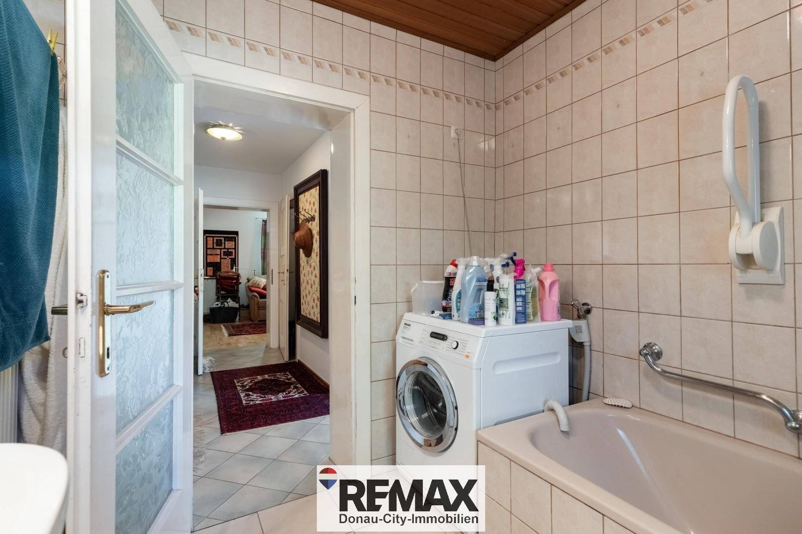 Praktischer Waschbereich mit Waschmaschine und Badewanne in einem gefliesten Raum.