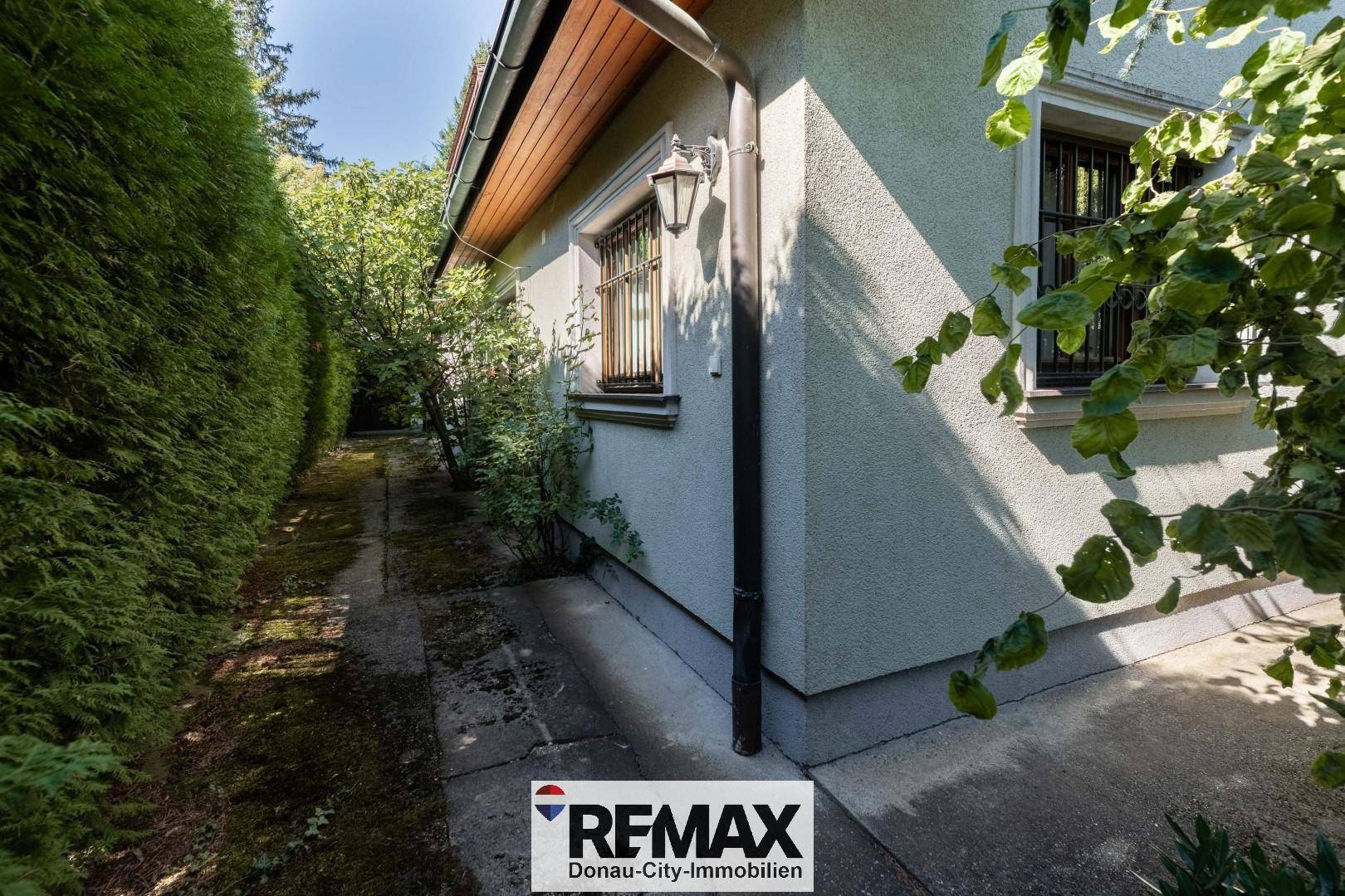 Seitenansicht des Hauses mit gepflastertem Weg und grüner Hecke.