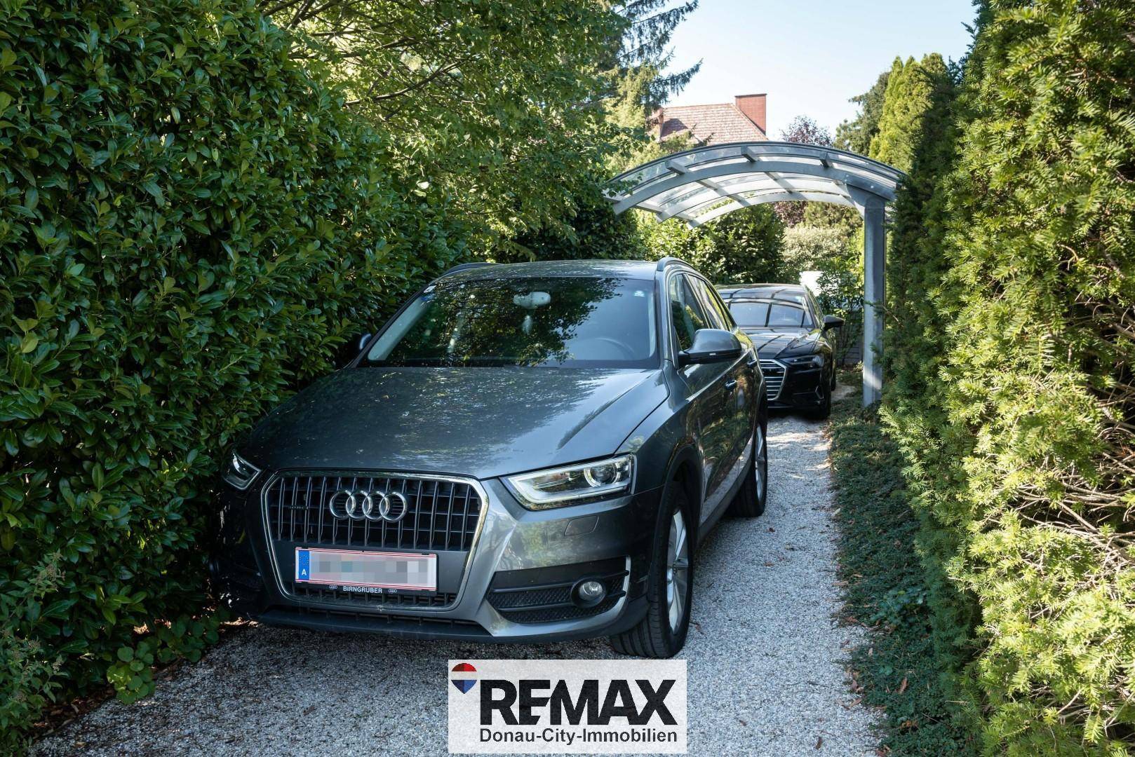 Überdachter Stellplatz für zwei Fahrzeuge, umgeben von hohen Hecken.