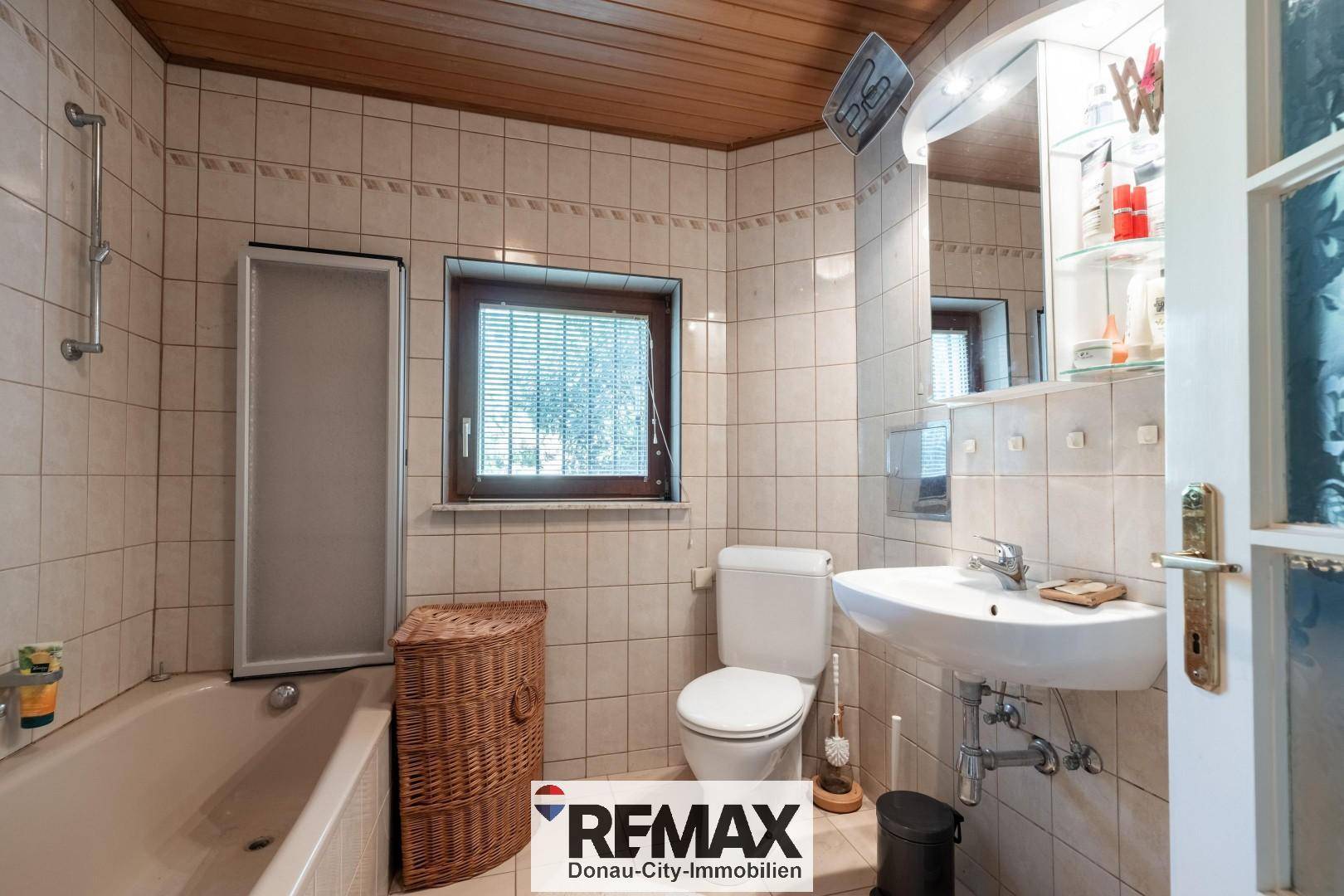 Gefliestes Badezimmer mit Badewanne, Waschbecken und Fenster für Tageslicht.