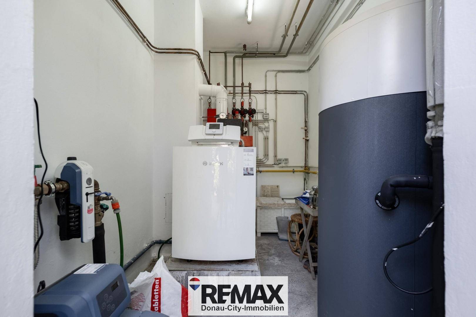 Technikraum mit Heizungsanlage, Warmwasserspeicher und sichtbaren Rohrleitungen.