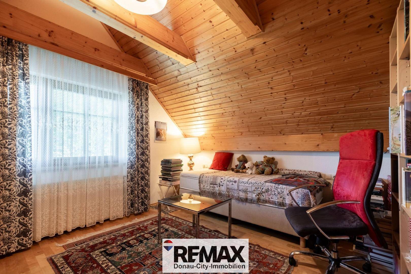 Helles Schlafzimmer im Dachgeschoss mit Holzvertäfelung, Fenster und Teppich.