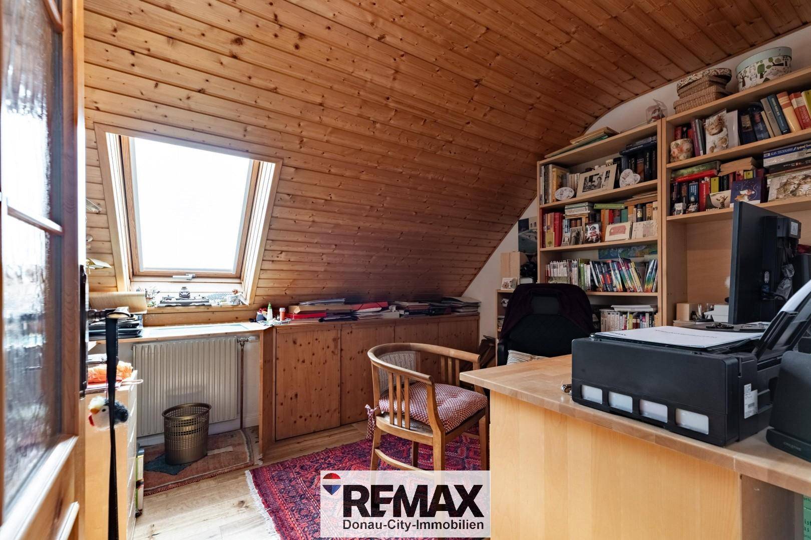 Helles Arbeitszimmer im Dachgeschoss mit Holzvertäfelung, Dachfenster und Bücherregalen.