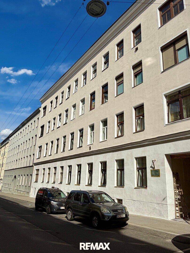 Klassische Fassade eines Mehrfamilienhauses an einer sonnigen Straße mit parkenden Autos.