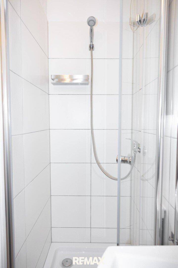 Moderne Duschkabine mit weißen Fliesen und Glasabtrennung in einem hellen Badezimmer.