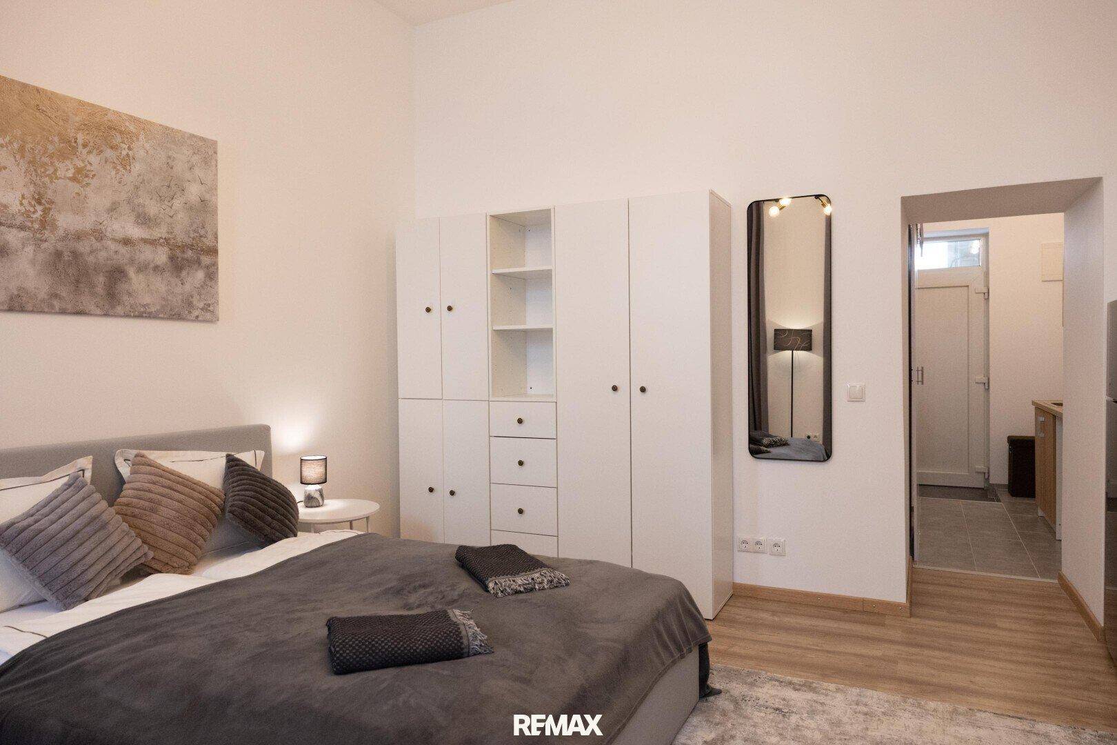 Schlafzimmer mit weißem Kleiderschrank und Blick in den Flur zur angrenzenden Küchenzeile.