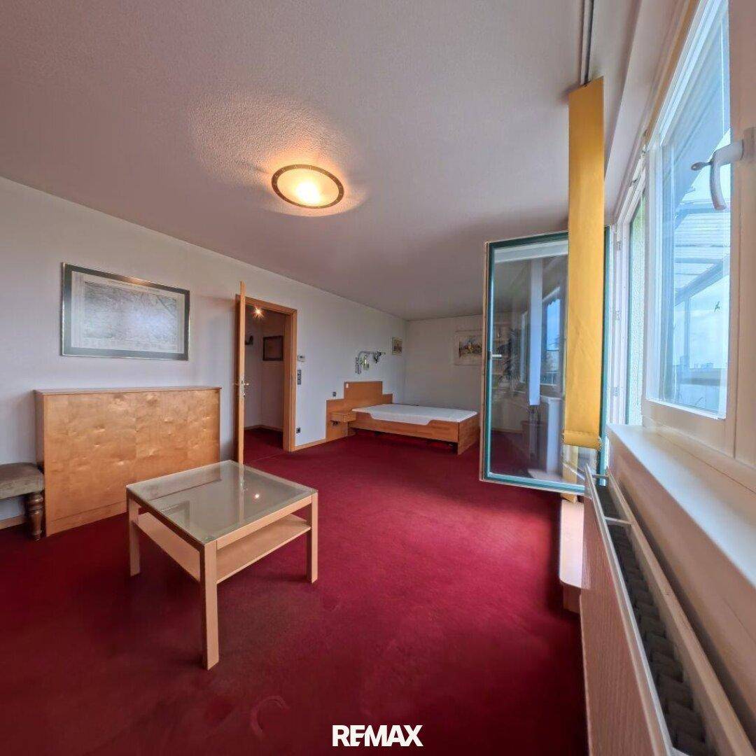 Schlafzimmer mit rotem Teppichboden, Bett und Zugang zu einem weiteren Raum.