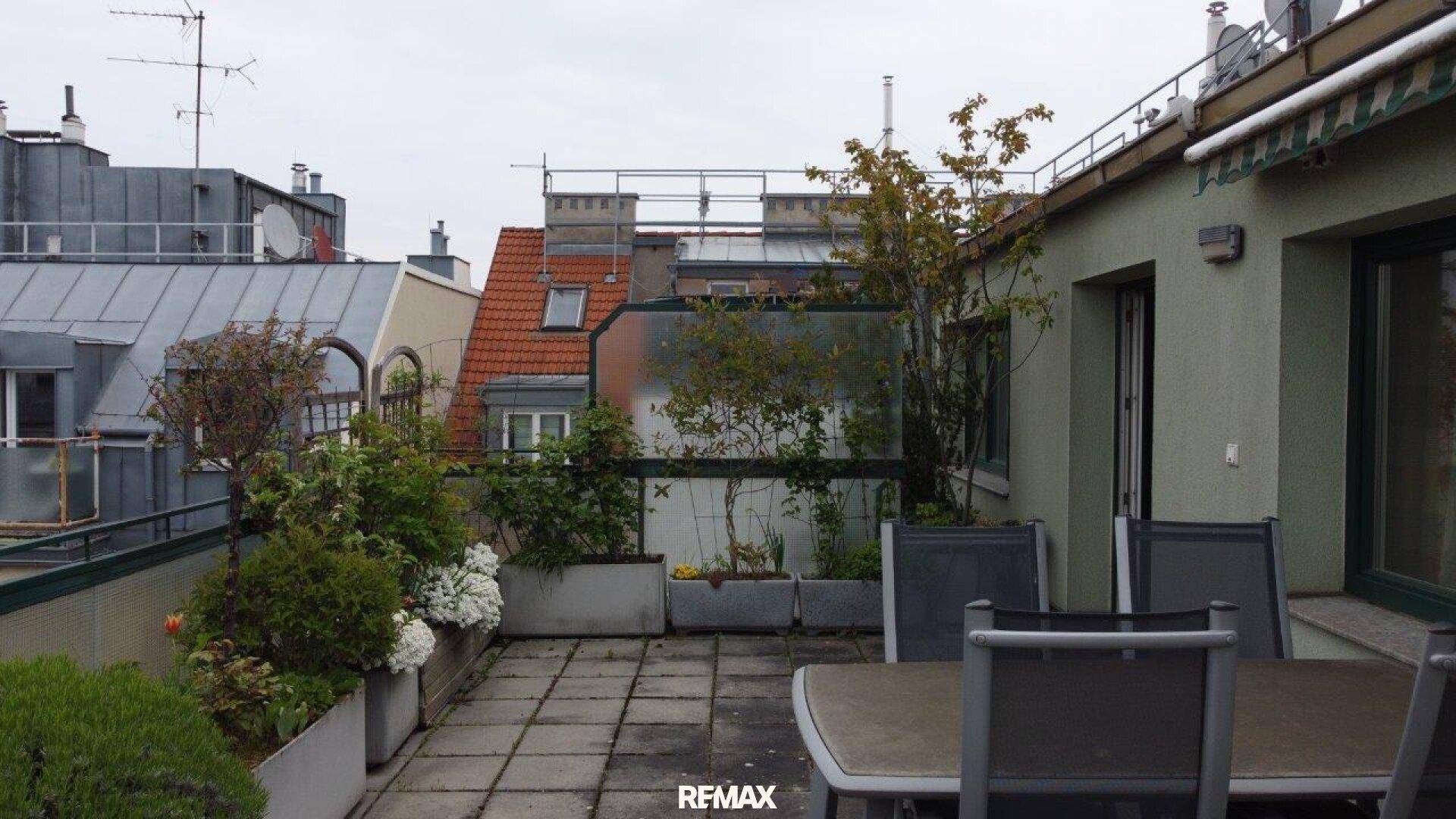 Dachterrasse mit Sitzgelegenheiten, Pflanzen in Kübeln und Blick auf umliegende Dächer.