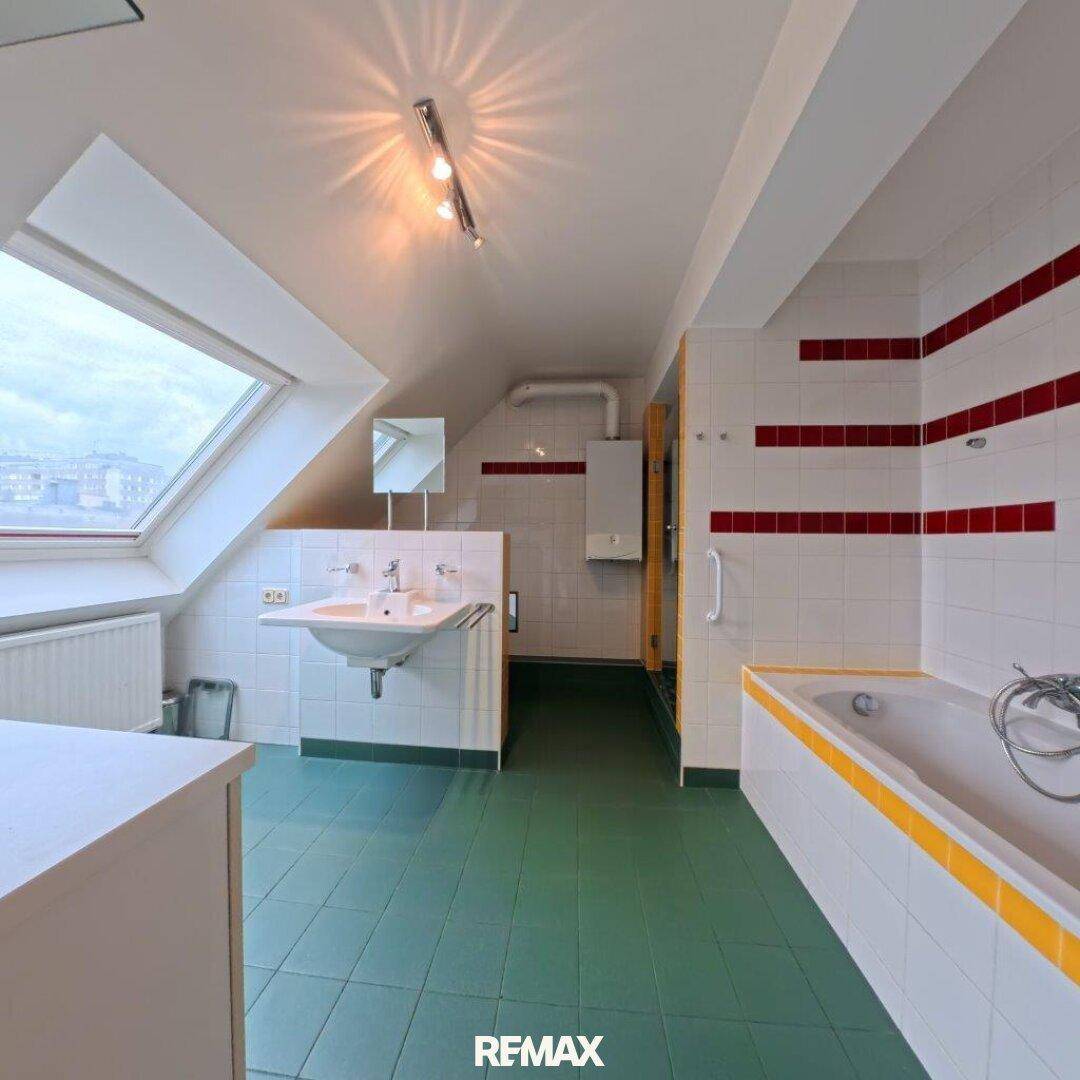 Helles Badezimmer im Dachgeschoss mit Dachfenster, Badewanne und grünem Fliesenboden.