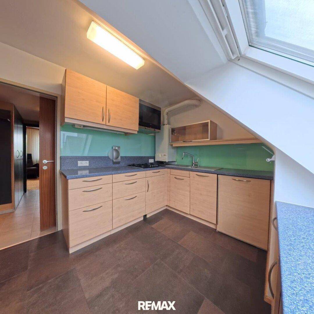 Einbauküche im Dachgeschoss mit Holzfronten, blauer Arbeitsplatte und Dachfenster.