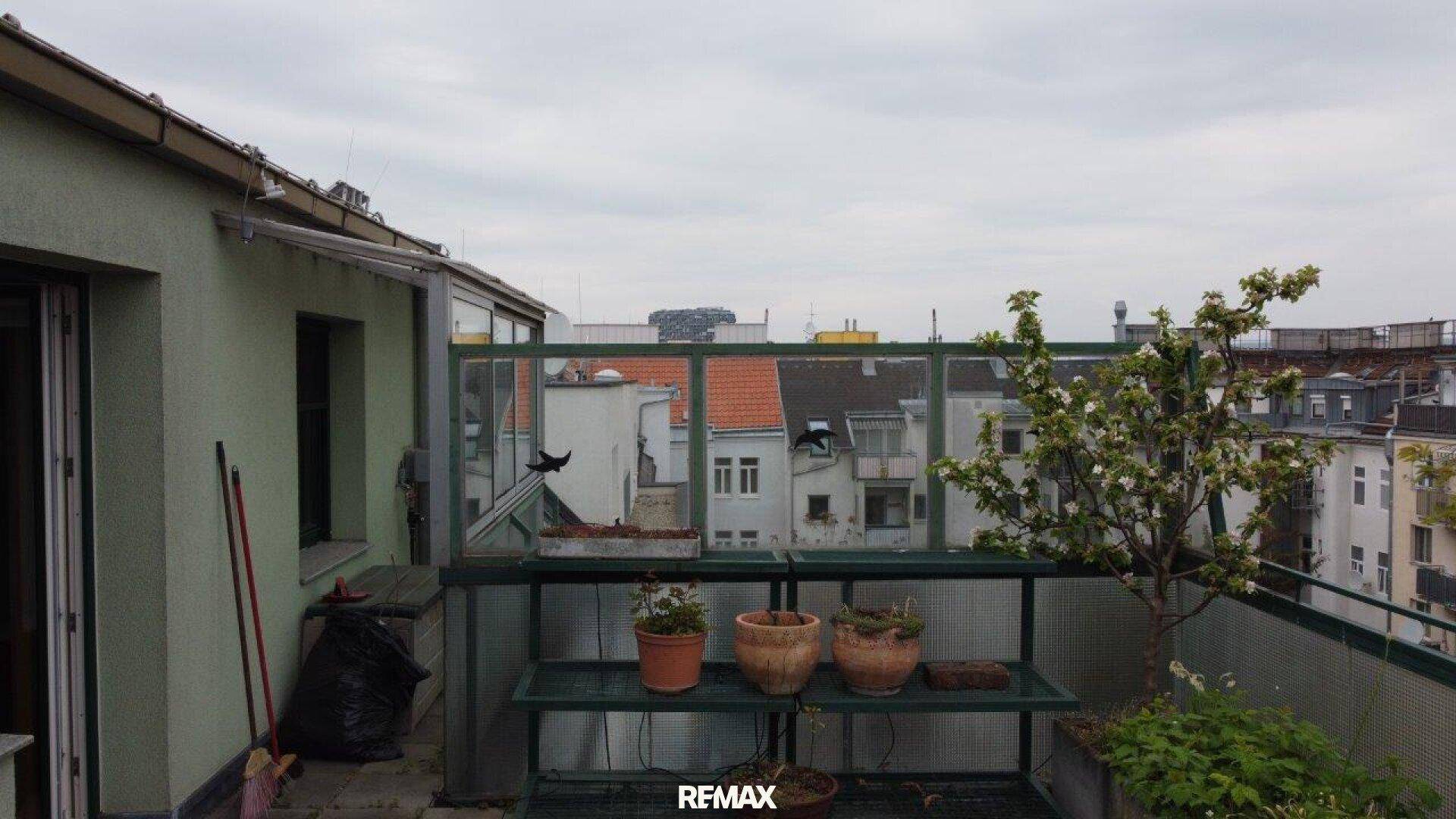 Balkon mit Pflanzen und Blick über die Dächer der Stadt an einem bewölkten Tag.