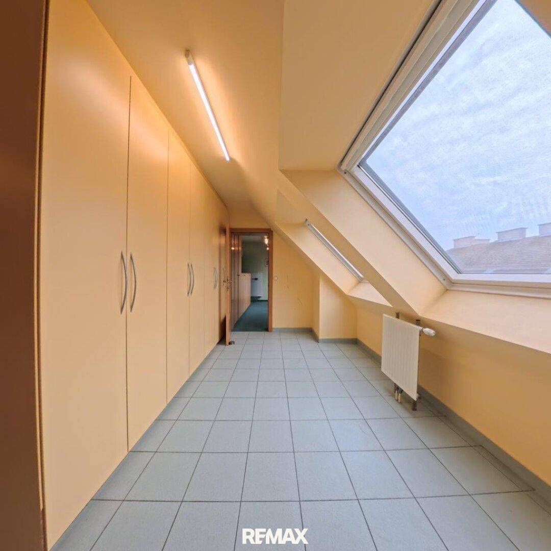 Dachgeschossraum mit Dachfenster, Fliesenboden und Einbauschränken entlang der Wand.
