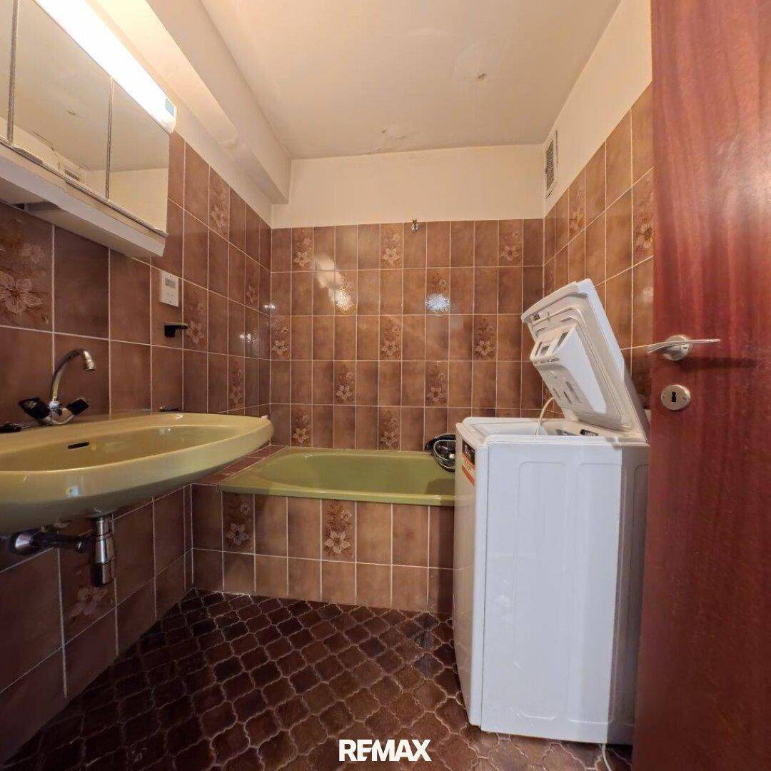 Badezimmer mit braunen Fliesen, Waschbecken, Badewanne und Waschmaschine.